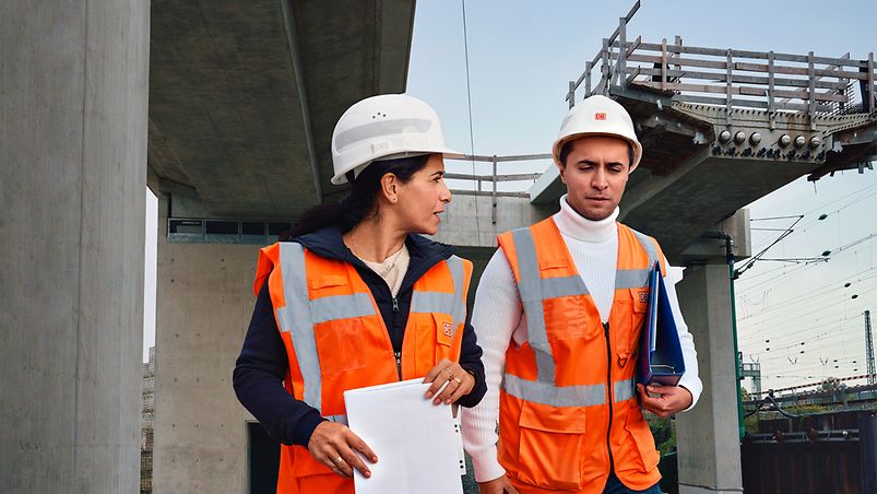 Eine Frau und ein Mann in DB Baubekleidung besprechen sich an einer Brückenbaustelle